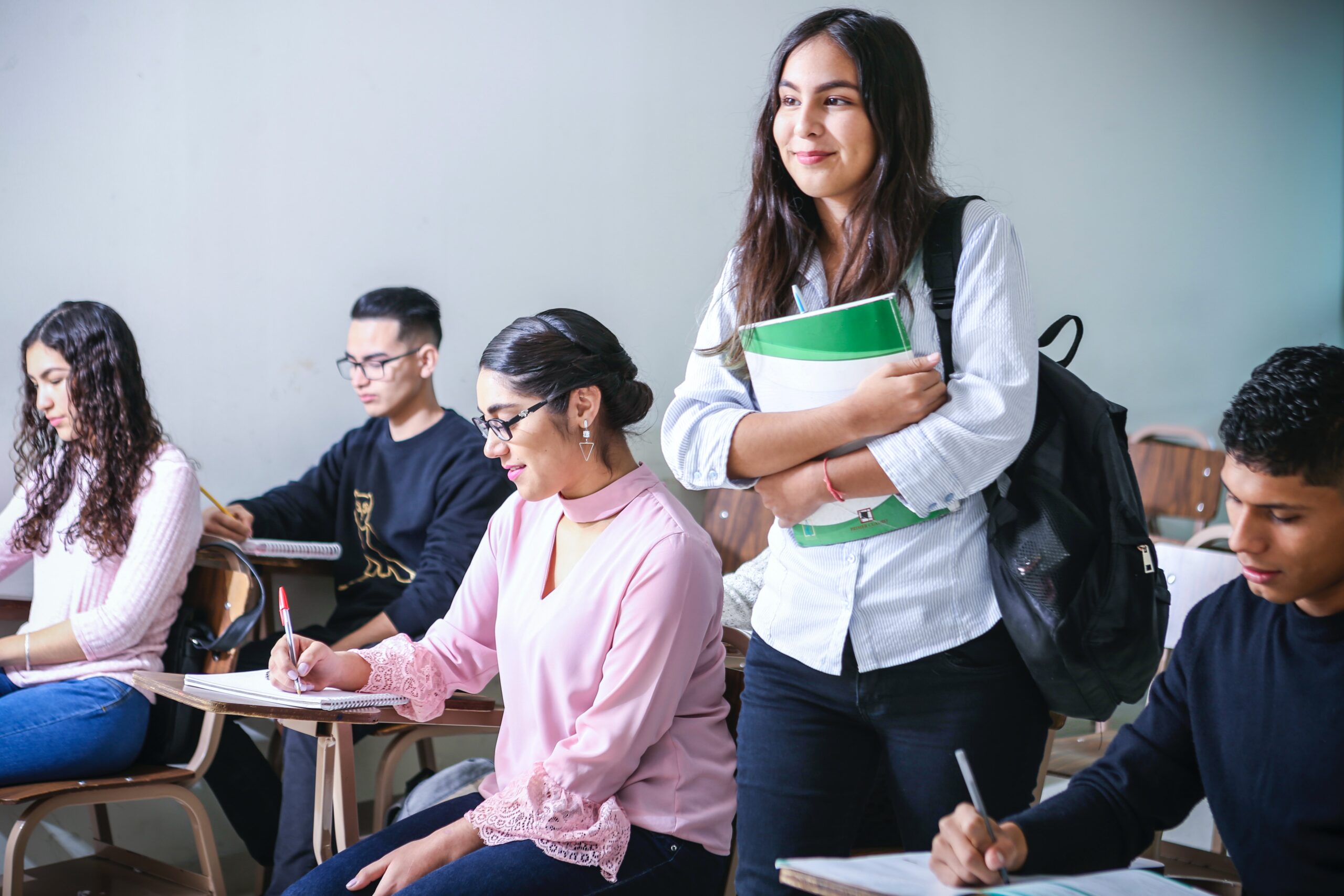 Student takes seat in class full of peers taking notes.